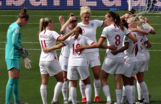 England women’s football players grouped on a pitch.