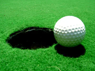A golf ball beside a hole on a putting green.