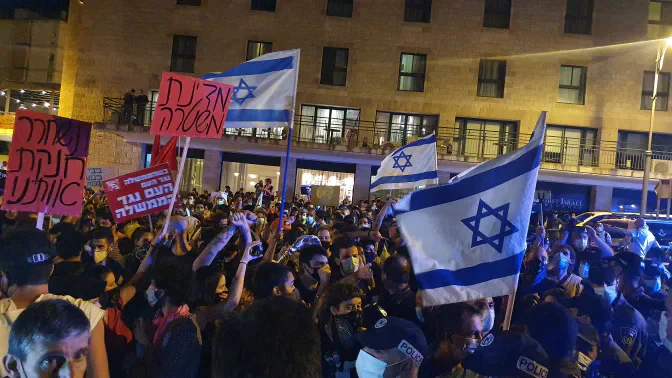 A night-time protest with Israeli flags and placards.