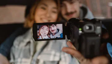 People posing together in front of a video camera, with their image visible on its screen.