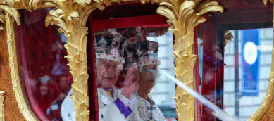 King Charles III and Queen Camilla riding in a gilded carriage during the coronation.