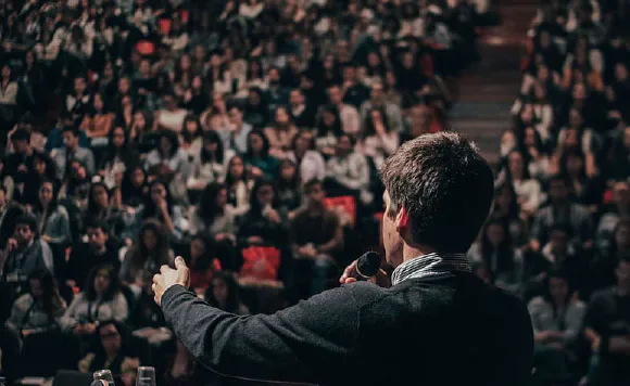 A speaker addressing a large audience from a stage.