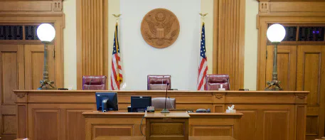 An empty courtroom bench with United States flags.
