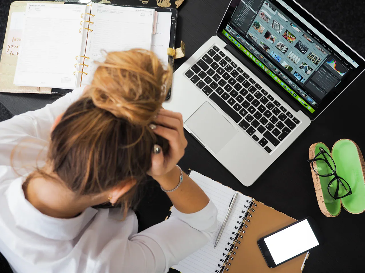 A student holding their head over notebooks beside a laptop.
