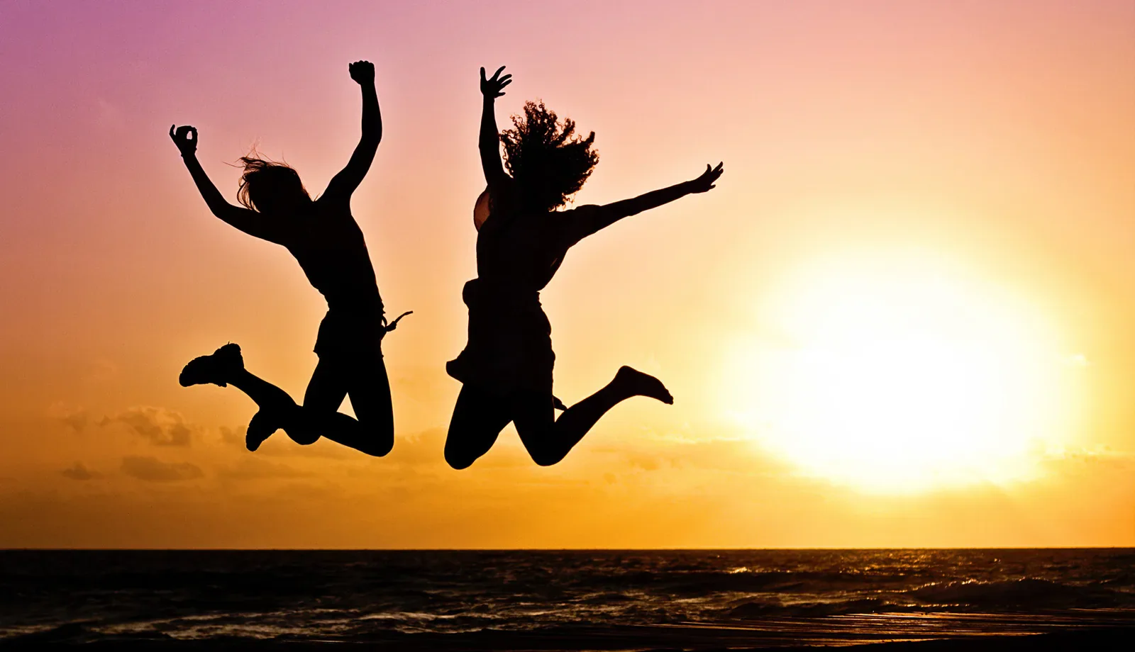 Two people jumping in silhouette against a sunset over the sea.