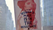 A poster reading “A woman’s place is in the resistance” displayed in a city window.