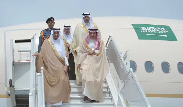 Saudi officials descending aircraft stairs beside a Saudi Arabian plane.