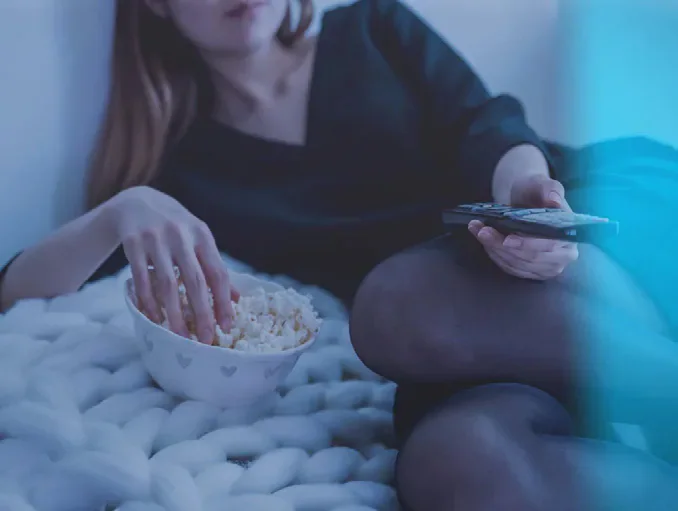 A person watching television with a remote control and bowl of popcorn