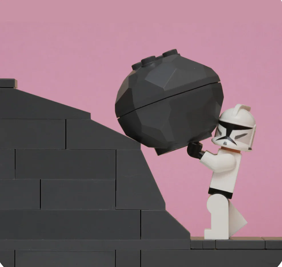 A Lego figure pushing a large black boulder up steps