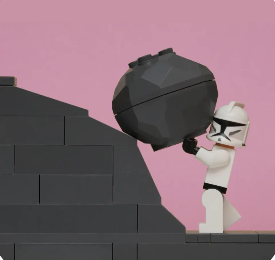 A Lego figure pushing a large black boulder up steps