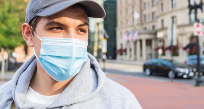 A young man wearing a blue surgical mask on a city street