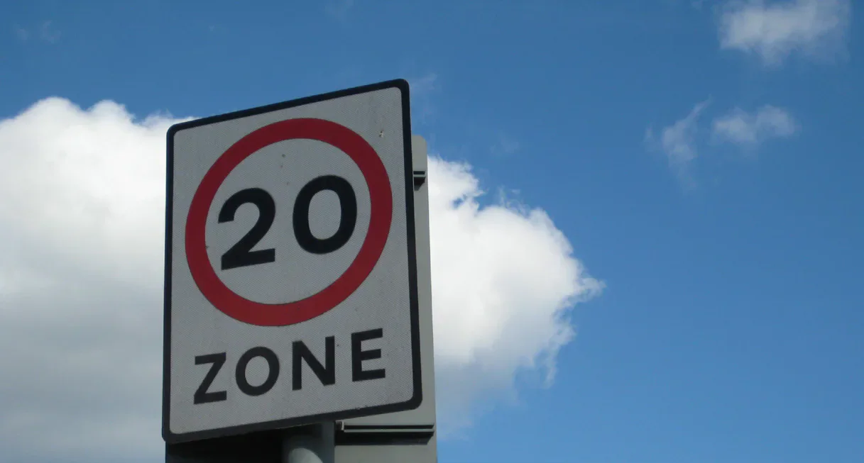A roadside sign marking a 20 mph zone against a blue sky