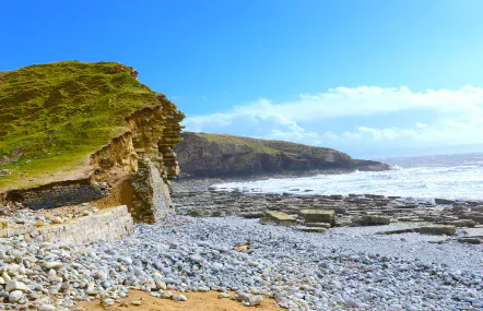 Rocky Welsh coastline beneath green cliffs and a blue sky