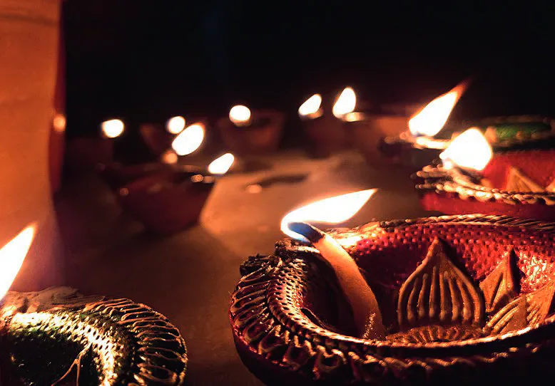 Rows of decorated clay oil lamps burning in a dark setting