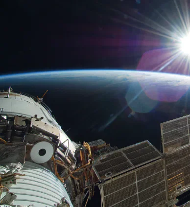 The International Space Station seen in orbit with sunlight flaring at the edge of Earth