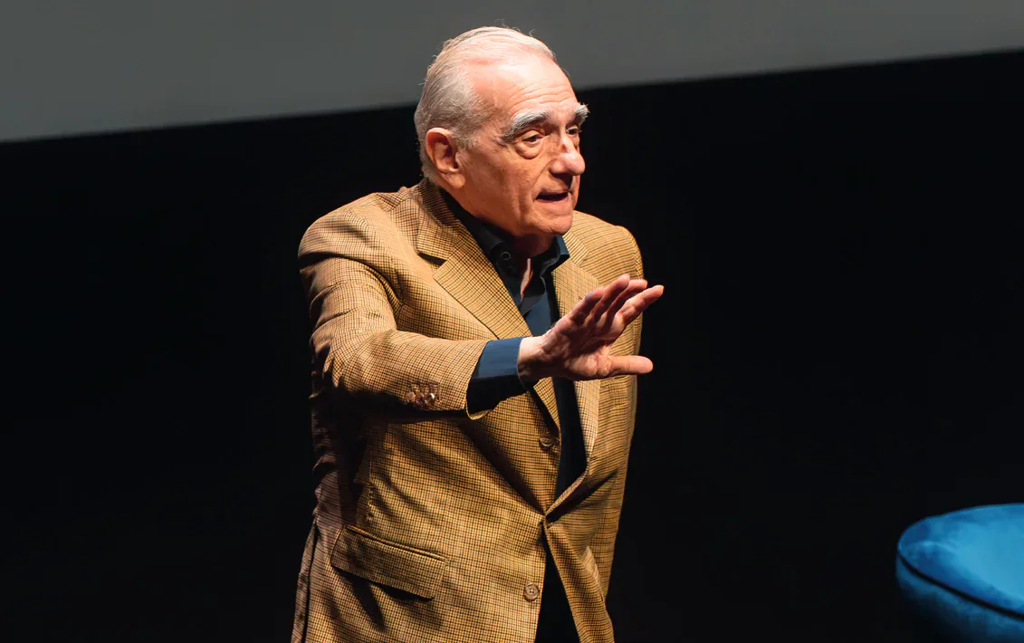 Martin Scorsese speaking on stage with one hand raised