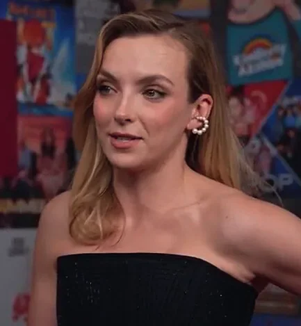 Jodie Comer in a black strapless dress speaking during an interview
