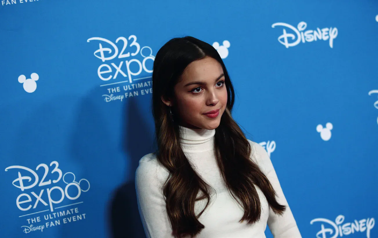 Olivia Rodrigo in front of a blue Disney D23 Expo backdrop