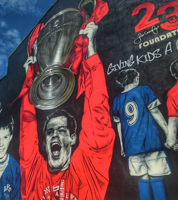 A Liverpool football mural showing a player lifting a trophy beside painted shirts and the words giving kids a chance