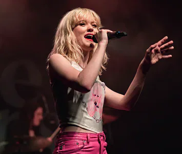 Maisie Peters performing on stage with a microphone