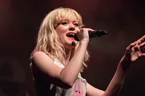 Maisie Peters performing on stage with a microphone