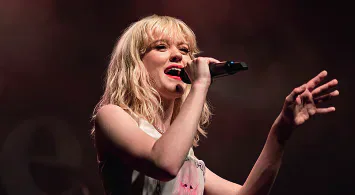 Maisie Peters performing on stage with a microphone