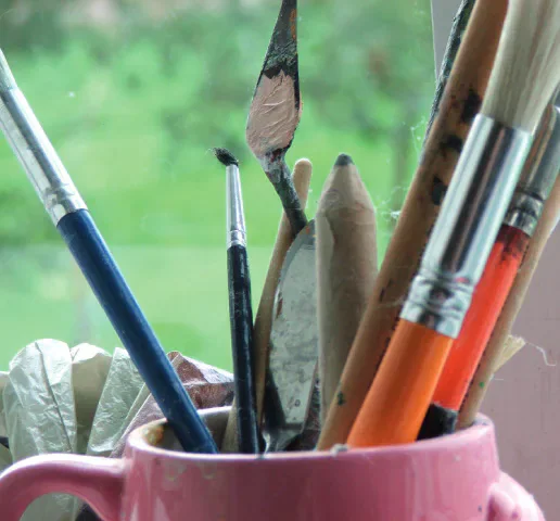 Paintbrushes and pottery tools in a pink mug