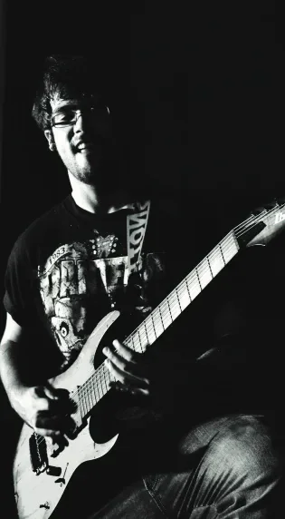 A guitarist performing under dark stage lighting.