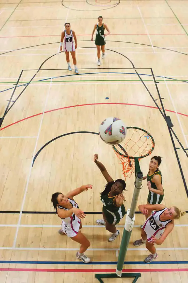 Netball players competing beneath a goal.