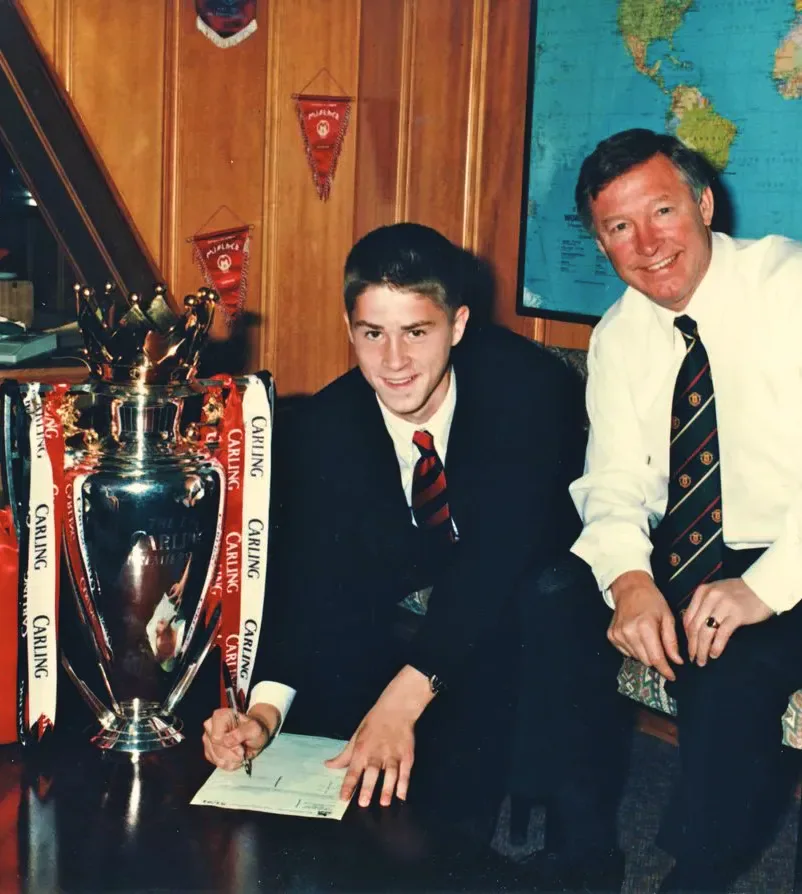 A young Rhodri Jones signing for Manchester United beside Sir Alex Ferguson and a trophy.