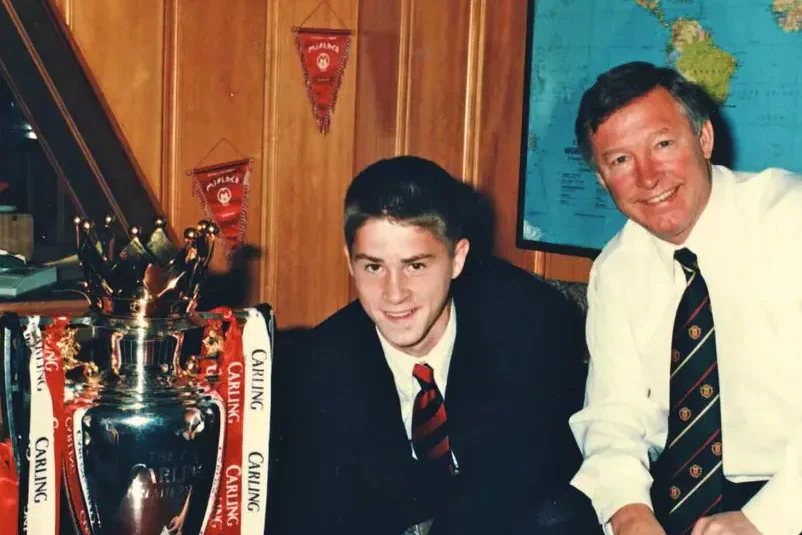 A young Rhodri Jones signing for Manchester United beside Sir Alex Ferguson and a trophy.