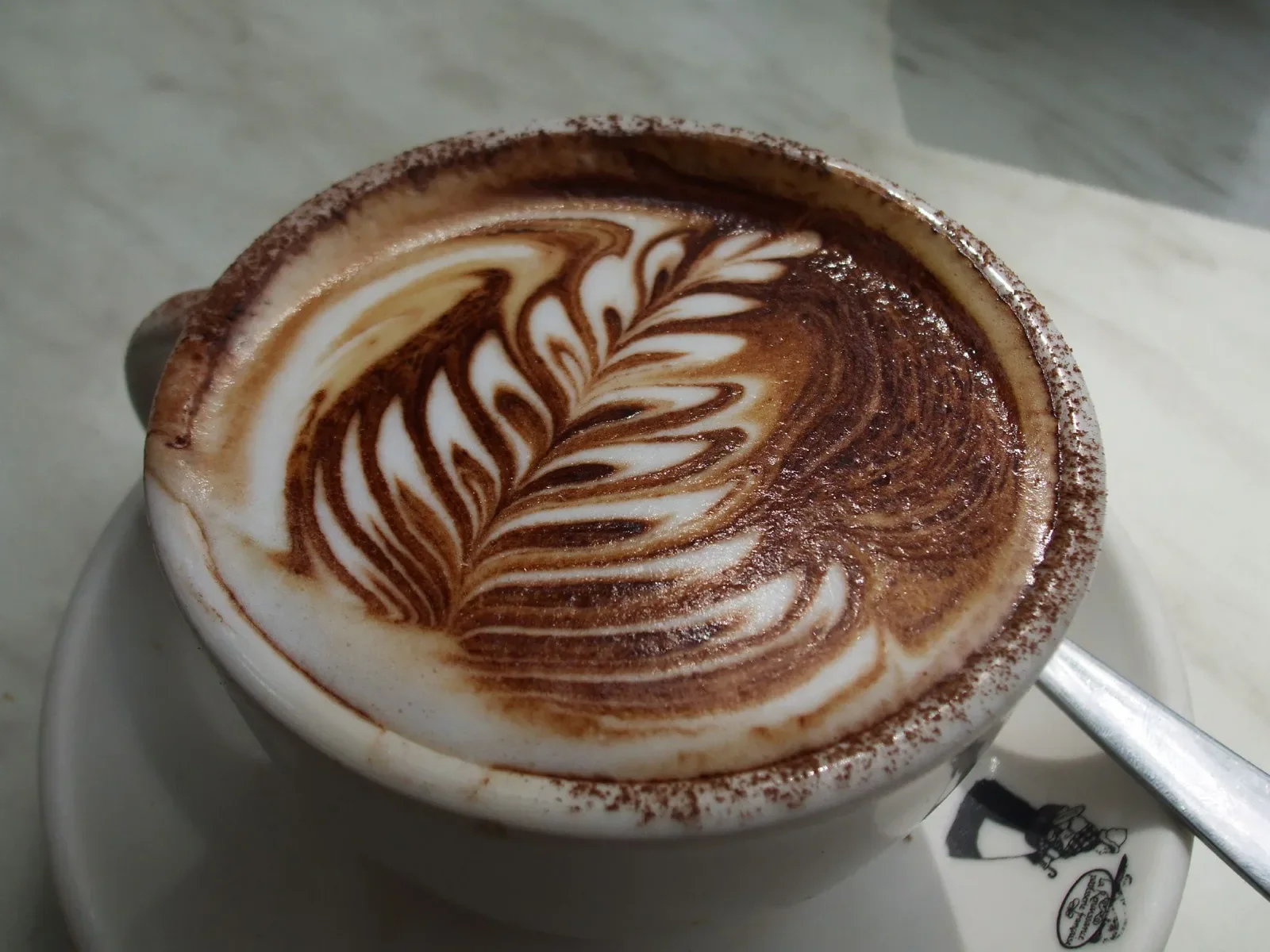 A close-up of a cup of coffee with leaf-shaped latte art.