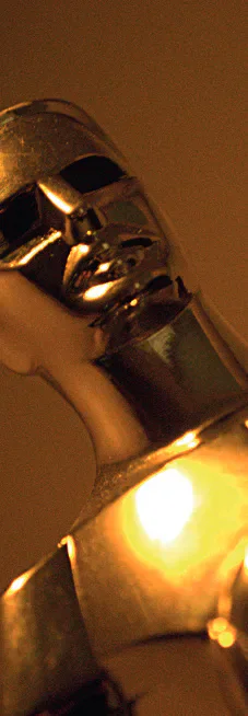A close-up of a gold Oscar statuette lit by warm light.