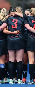 A women's sports team gathers in a huddle on the pitch.