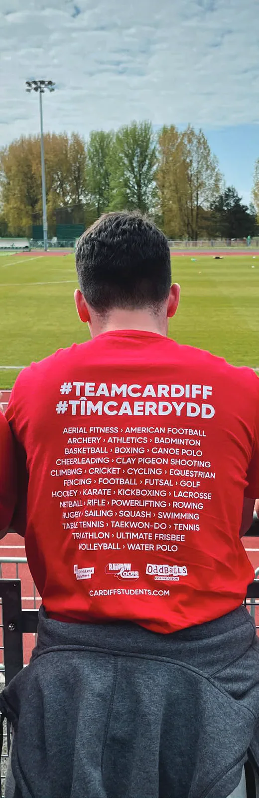 Back of a red Team Cardiff shirt beside an athletics track