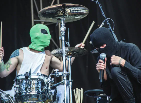 Twenty One Pilots performing in masks beside a drum kit