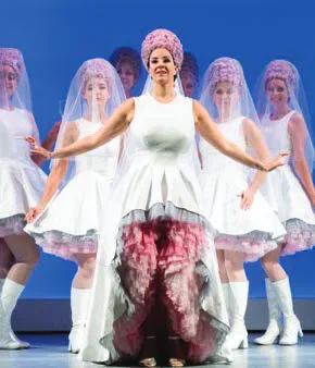 An opera singer in a white costume with dancers behind her