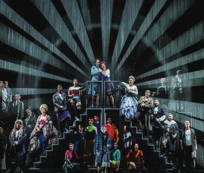 Welsh National Opera cast posed on a staircase beneath radiating stage lights