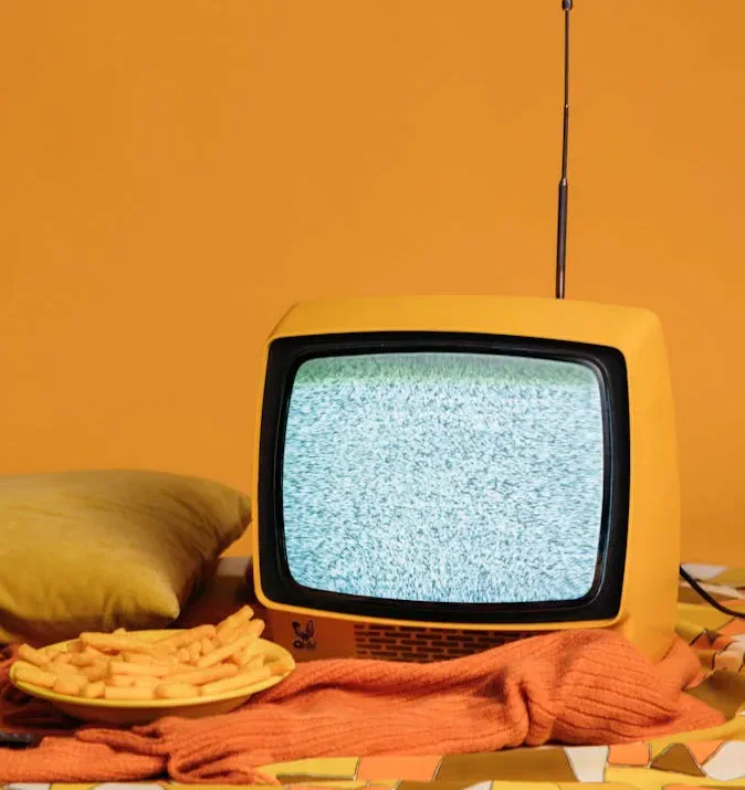 A yellow vintage television showing static beside a plate of chips.