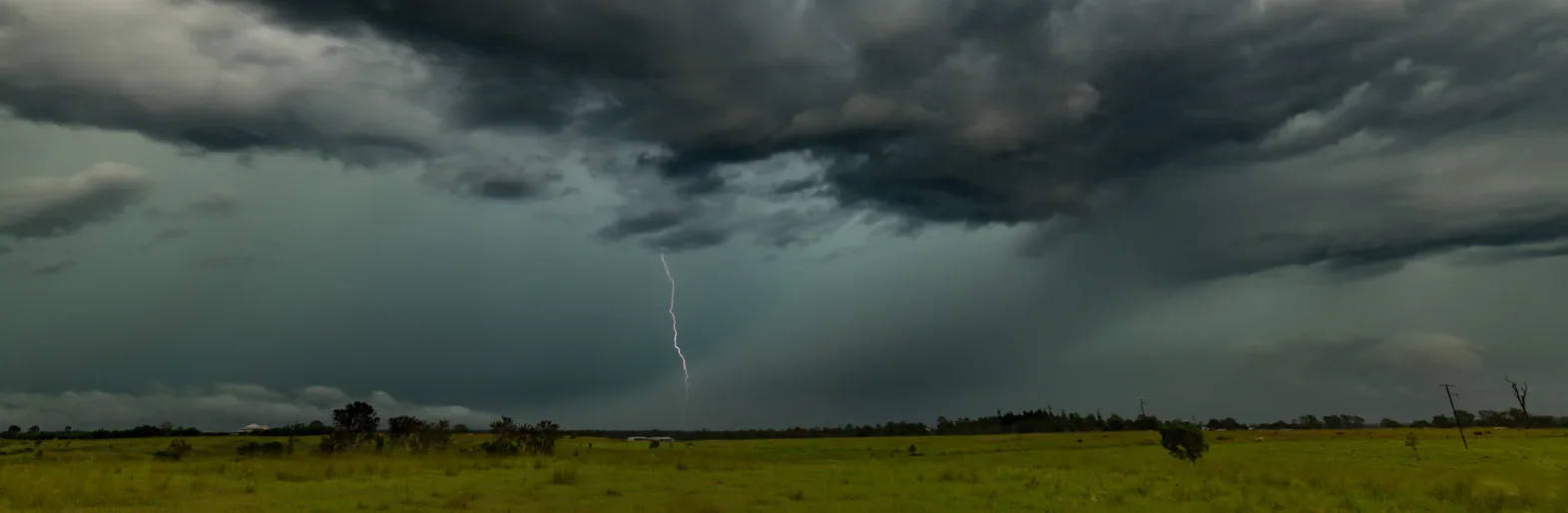 Lightning beneath dark storm clouds over open countryside.