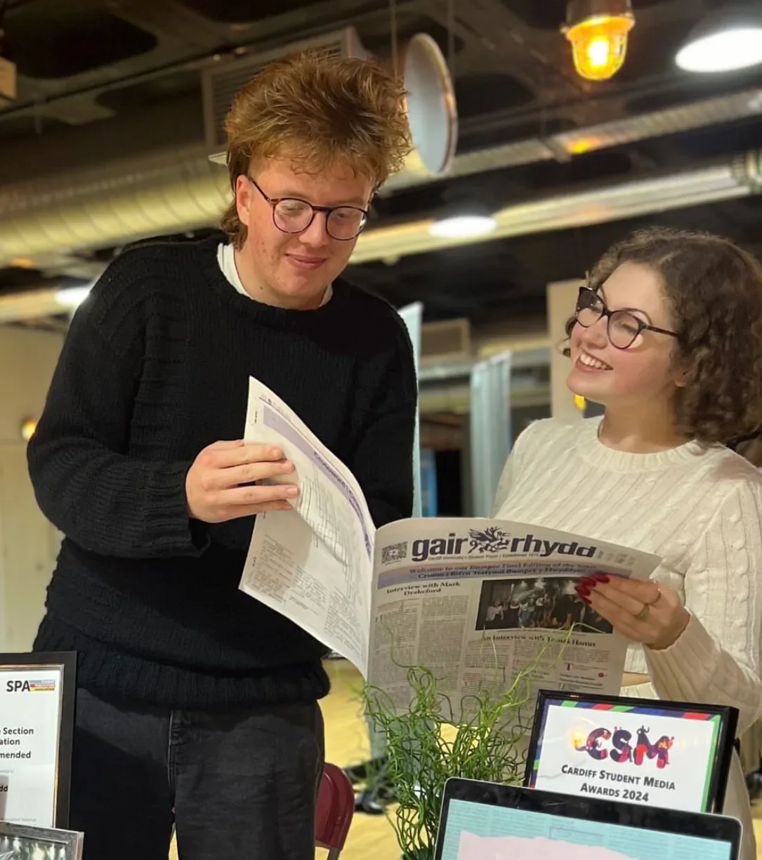 Two students reading a copy of Gair Rhydd at the Freshers’ Fair stand.