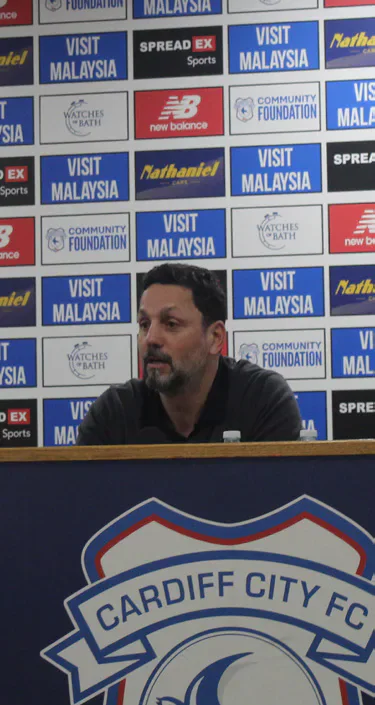 A Cardiff City manager speaking at a press conference behind the club crest.