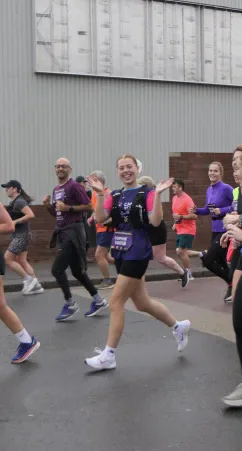 Sophie Pask smiling and waving while running the Cardiff Half Marathon.