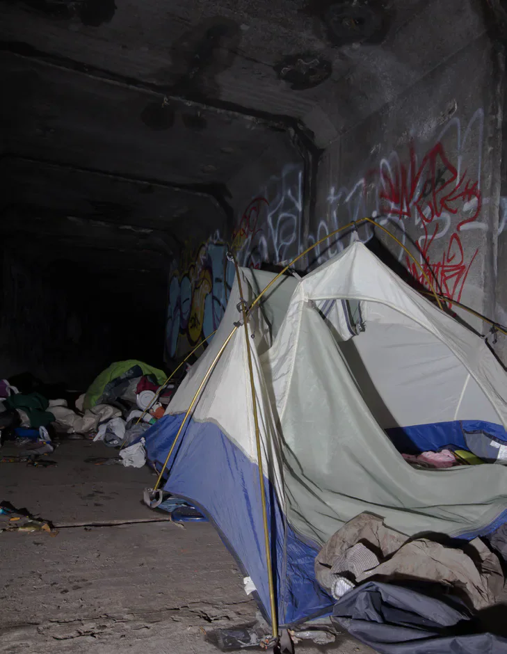 A tent and belongings in a graffiti-covered concrete shelter.