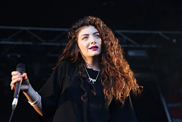 Lorde performing on stage with a microphone.