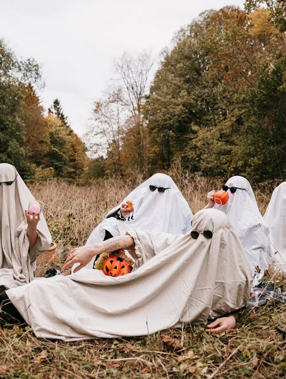 A group dressed as sheet ghosts relaxing outdoors in autumn.