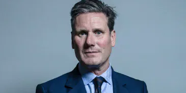 Keir Starmer standing in a blue suit against a plain grey background.