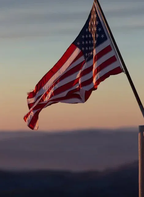The United States flag flying against a sunset sky.