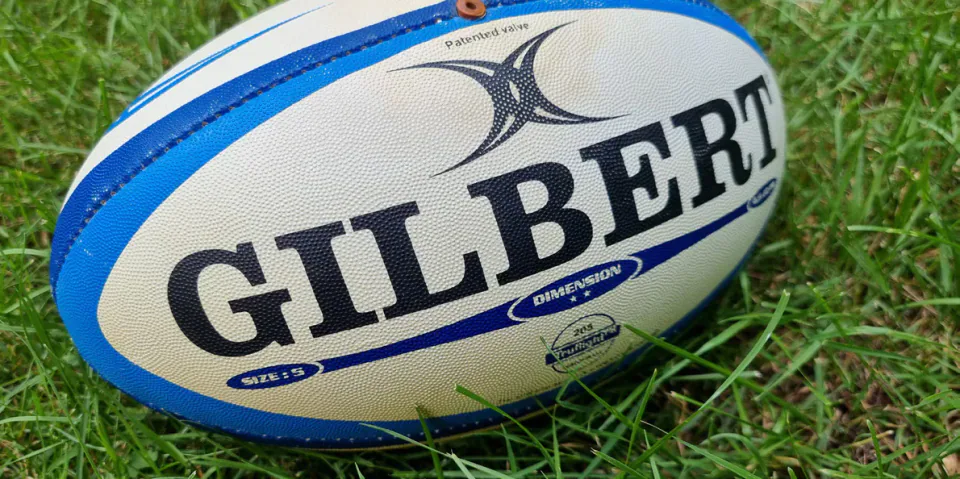 A blue-and-white Gilbert rugby ball resting on grass.