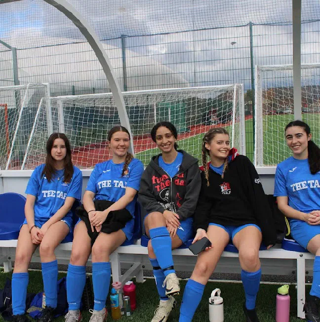 Five Cardiff University Ladies Football players seated together in the dugout.